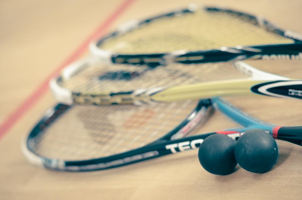 Two squash rackets and two black squash balls on the floor of a squash court